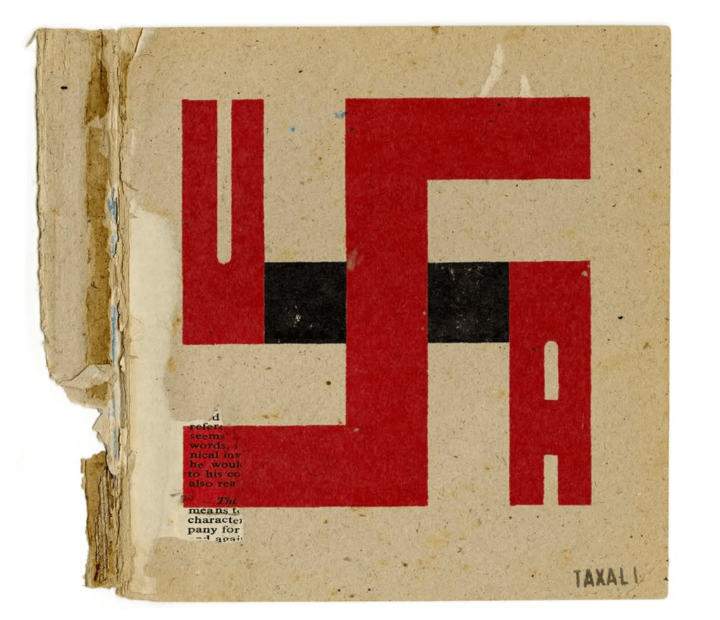 An illustration on a piece of recycled cardboard of a swastika with red letters "U S A" forming its shape. 